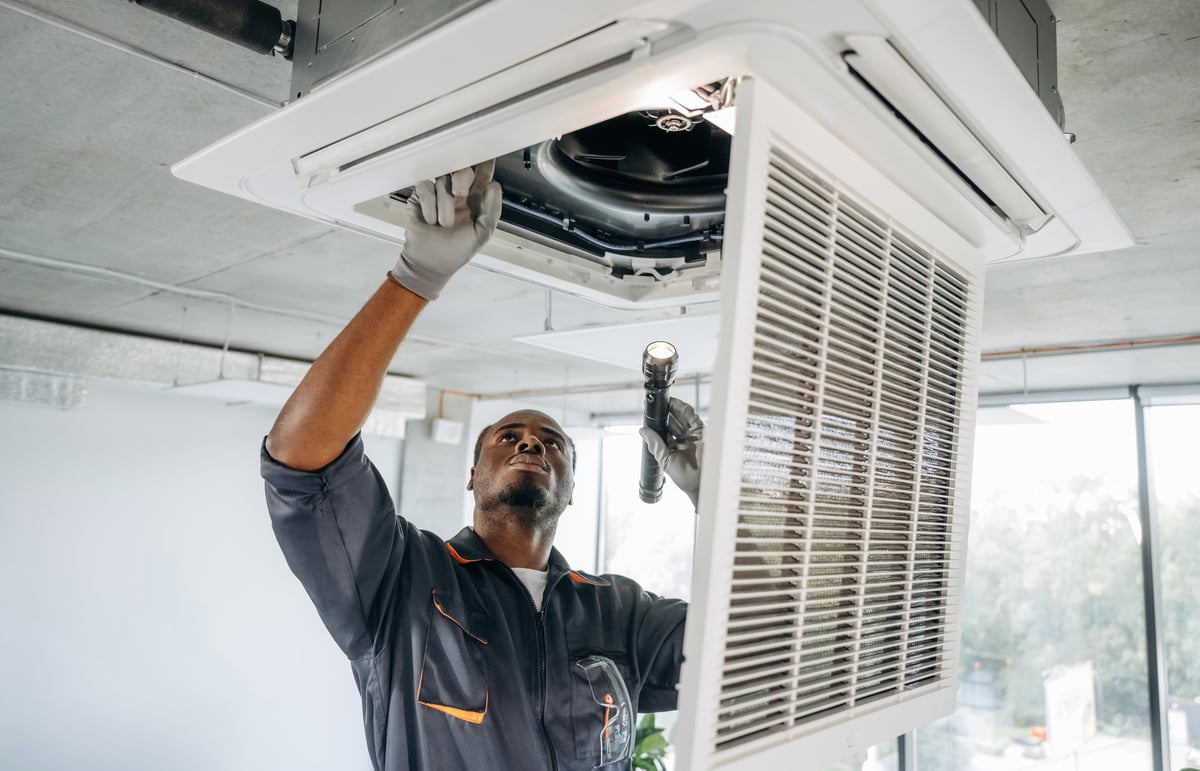 Técnico reparando un sistema de ventilación en una oficina moderna