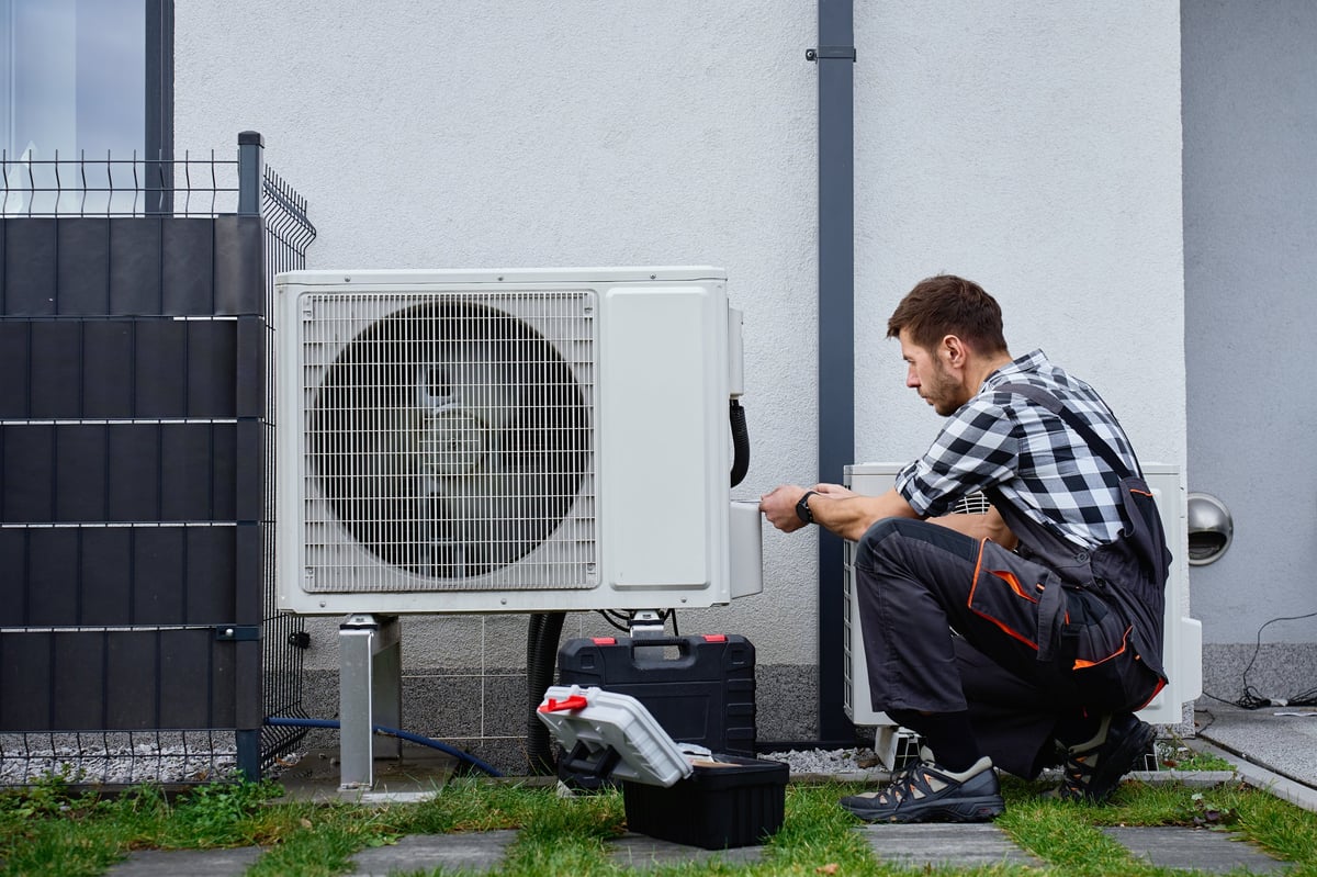 Técnico realizando mantenimiento a una unidad de bomba de calor en el exterior de una casa